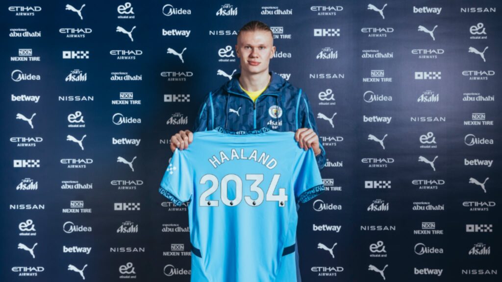 Erling Haaland holding up a shirt with contract until 2034 on it